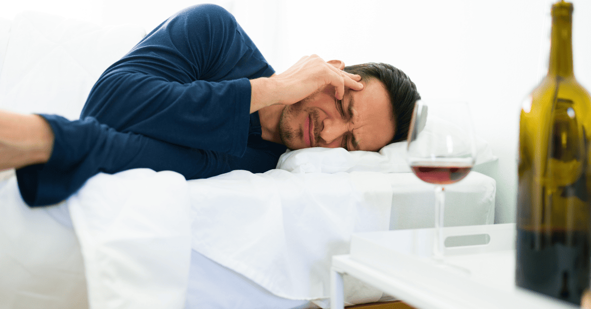 Pessoa deitada com ressaca ao lado de uma garrafa de vinho.